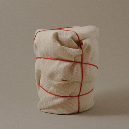 Hand-wrapped luxury candle, sculptural design wrapped in raw canvas wrapping with a red string from Mothers Milk.